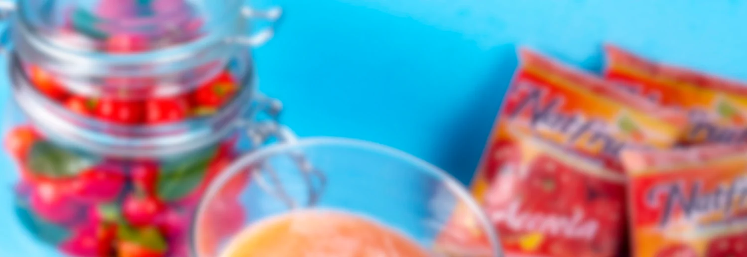Imagem desfocada de suco, frutas em um pote e polpas sobre uma mesa com fundo azul